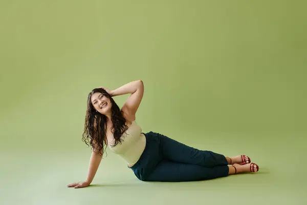 A confident young woman showcases her beauty in a corset, exuding joy against a vivid green setting. — Stock Photo