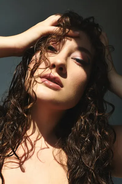 Una giovane donna sicura di sé con i capelli ricci posa con grazia in un ambiente grigio studio. — Foto stock