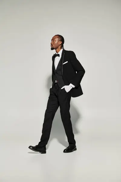 A stylish young man dressed in a tailored suit and vest walks with poise against a neutral backdrop. — Stock Photo