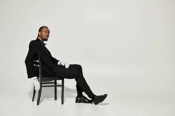 A young African American man elegantly dressed in a suit and vest sits confidently on a chair, showcasing style. — Stock Photo