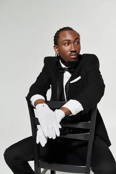 A stylish young man exudes sophistication while poised on a chair, dressed in a classic suit and gloves. — Stock Photo