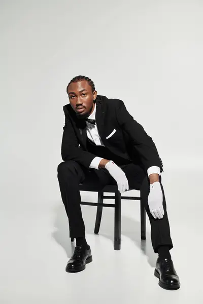 A dapper young man in a tailored suit sits on a chair, exuding elegance against a soft grey background. — Stock Photo