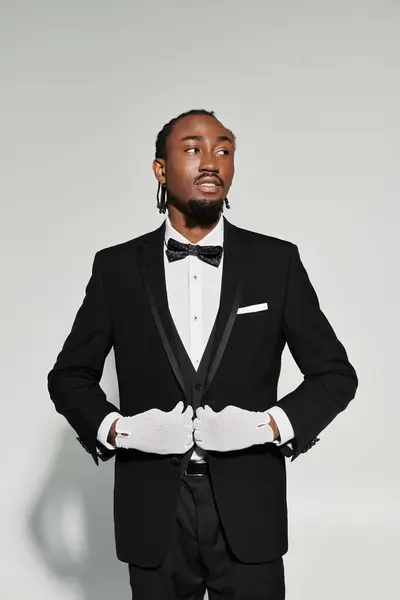 A poised young man dressed in a stylish suit and gloves confidently poses against a soft grey background. — Stock Photo