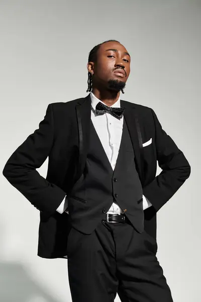 A young man dressed in a sharp suit and vest stands proudly on a grey background, exuding confidence and elegance. — Stock Photo