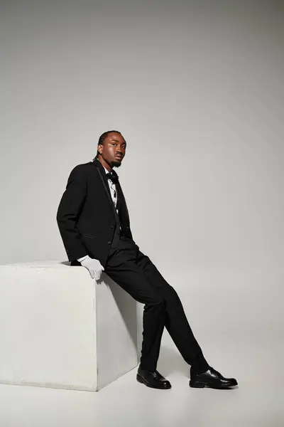 A young Black man in a tailored suit and vest poses elegantly against a grey backdrop. — Stock Photo