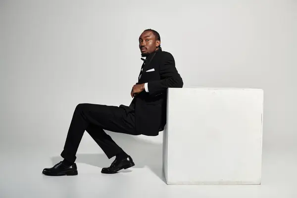 A stylish young man dressed in a sharp suit strikes a poised pose against a smooth grey background. — Stock Photo