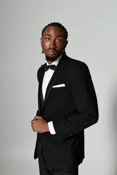 A stylish young man dressed in a sharp suit and bow tie exudes confidence against a minimal grey background. — Stock Photo