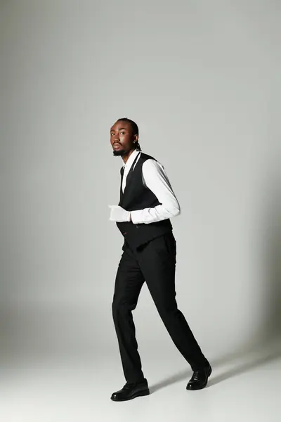 A young African American man stands poised in a tailored suit, showcasing elegance and style with a grey background. — Stock Photo