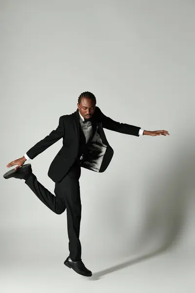 A confident young man in a tailored suit strikes a dynamic pose against a minimalist grey background. — Stock Photo