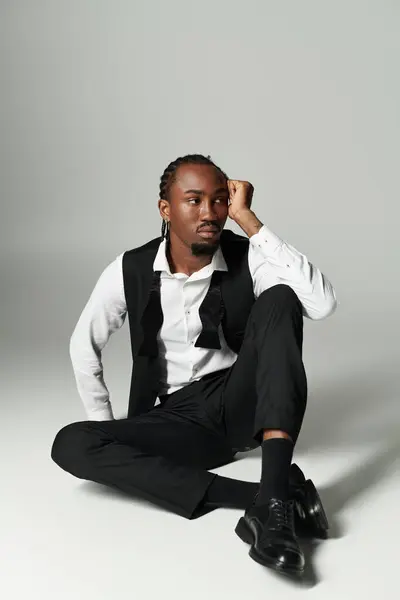 Dressed in a sharp suit, a young man reflects while seated casually on a grey background, exuding confidence. — Photo de stock