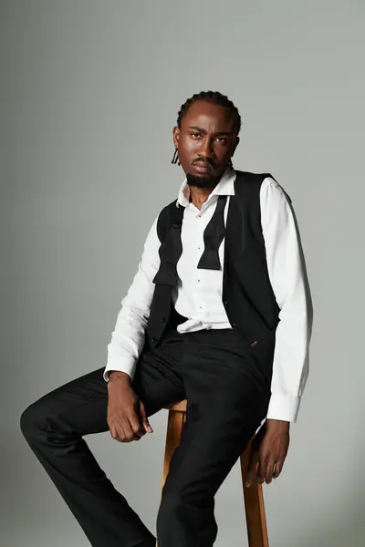 A young man exudes confidence in a black suit and vest, striking a pose with attitude on a grey background. — Stock Photo