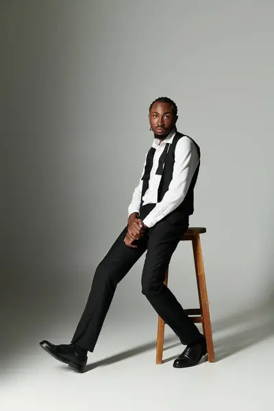 A young Black man in a tailored suit sits confidently on a stool in a minimalistic setting. — Stock Photo