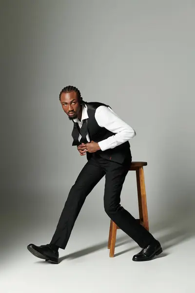A young man dressed in a sharp suit and vest confidently poses on a stool, showcasing elegance and style. — Stock Photo