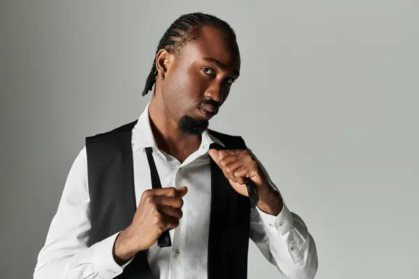 A young African American man dressed in a sharp suit adjusts his attire while exuding confidence on a grey backdrop. — Stock Photo