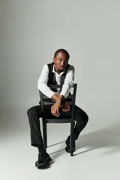 A young African American man in a stylish suit exudes confidence while seated on a chair against a grey background. — Stock Photo