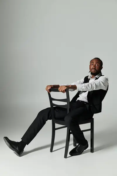 A young man in a sharp suit confidently sits on a chair, emanating elegance and poise in a minimalist setting. — Stock Photo