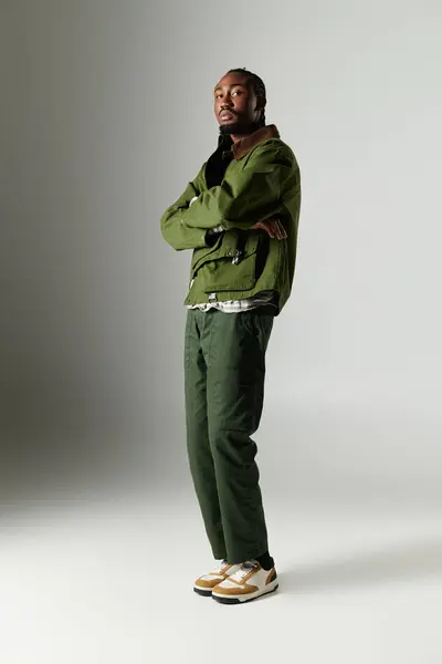 A young man stands poised on a neutral backdrop, showcasing trendy green clothing and a fashionable demeanor. — Stock Photo