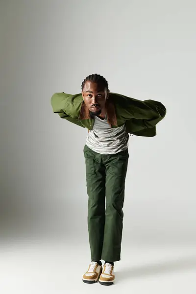 A fashionable young man showcases his unique style in green attire, confidently posing against a simple grey backdrop. — Stock Photo