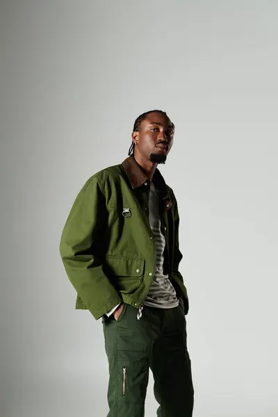 A young man confidently poses in stylish green attire, showcasing his unique fashion sense against a grey background. — Stock Photo