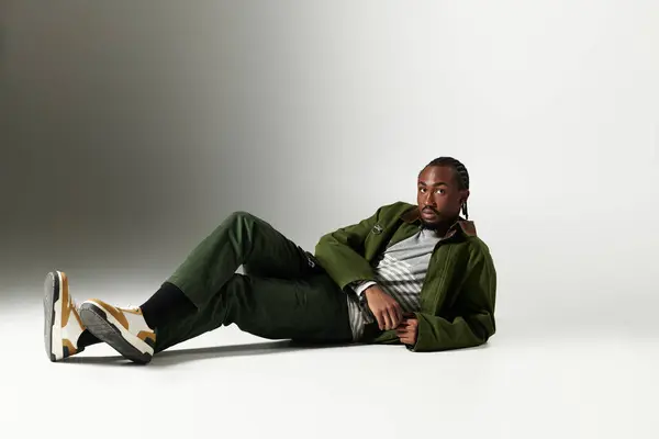 A fashionable young man lounges gracefully on the floor, showcasing his trendy green outfit with flair. — Stock Photo