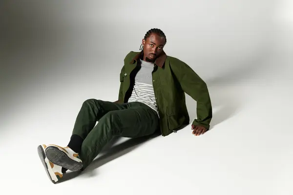 A young African American man showcases his trendy green outfit while seated on a smooth surface, exuding style. — Stock Photo