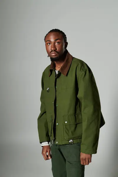 A young man with a keen fashion sense showcases his green outfit and striking presence against a grey wall. — Stock Photo