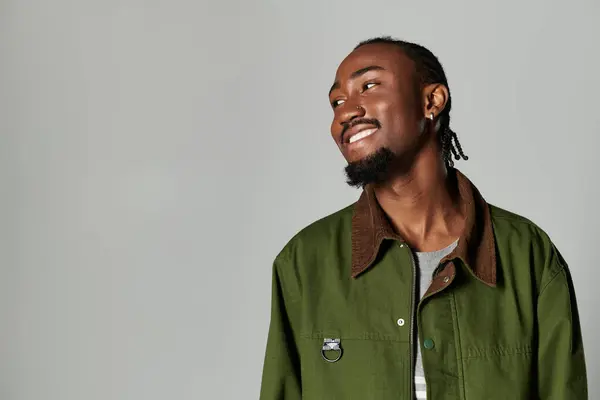A young African American man showcases his fashion sense in stylish green attire against a sleek grey backdrop. — Stock Photo