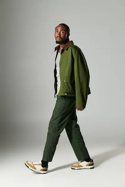 A young man dressed in a fashionable green ensemble strikes a confident pose on a neutral background. — Stock Photo