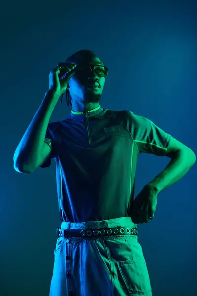 A young African American man strikes a confident pose in a neon-lit studio, radiating style and attitude. — Stock Photo