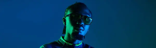 A confident young man in trendy attire stands in a studio, illuminated by colorful neon lights. — Stock Photo