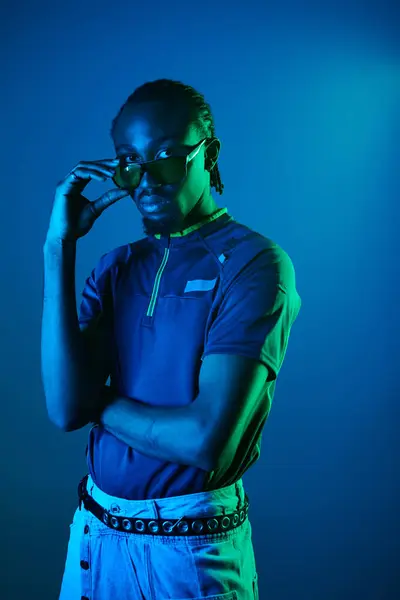 A young African American man showcases his unique style with confidence in a vibrant neon studio setting. — Stock Photo