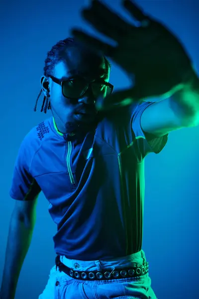 A young African American man in trendy attire strikes a dynamic pose against vibrant neon lights. — Stock Photo