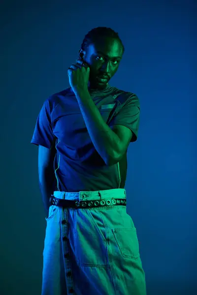 A young African American man showcases his unique style while posing in a studio illuminated by neon colors. — Stock Photo