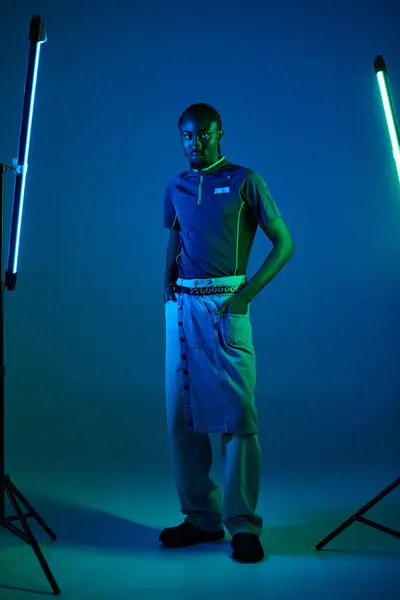 Un jeune homme présente sa tenue à la mode au milieu de lumières au néon vibrantes dans un cadre de studio dynamique. — Photo de stock