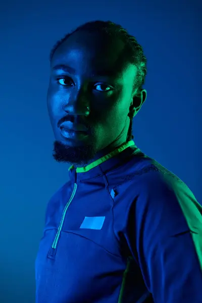A young man showcases his fashion sense in a trendy outfit, illuminated by striking neon hues in a studio. — Stock Photo