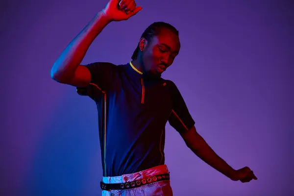 A young African American man dressed fashionably strikes a confident pose in a bright neon studio. — Stock Photo