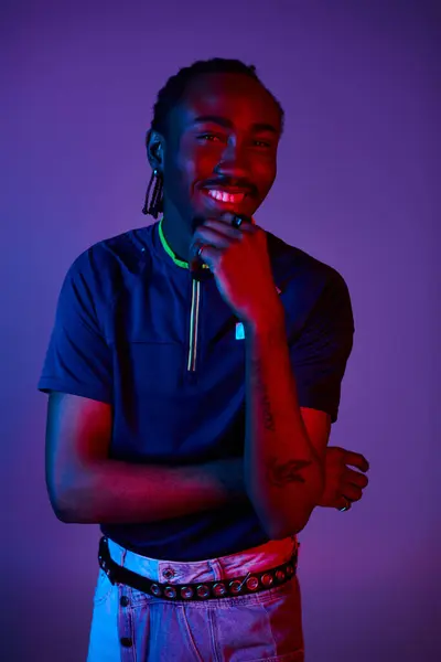 Un jeune homme afro-américain met en valeur son style unique tout en posant sous un éclairage au néon vibrant. — Photo de stock