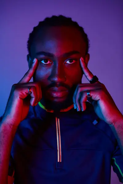 A young African American man strikes a pose in a stylish outfit, illuminated by vibrant neon lights. — Stock Photo