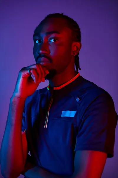 A young African American man showcases fashionable attire while striking a thoughtful pose in neon lighting. — Stock Photo