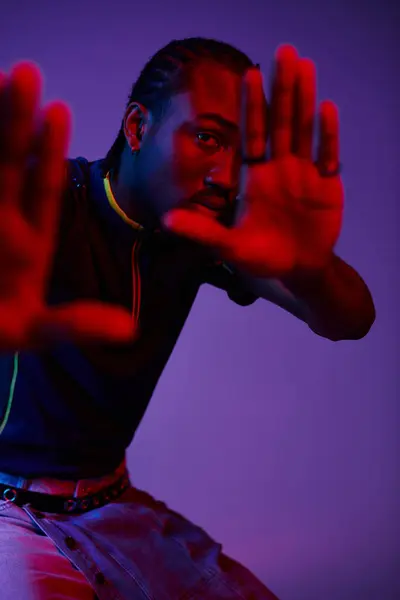 A young man shows his fashion flair with neon lighting while striking a confident pose in the studio. — Stock Photo