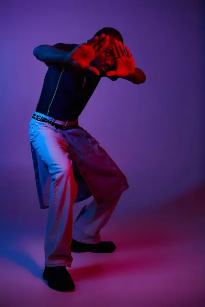 A fashionable young man confidently poses in a studio, illuminated by vibrant neon lights. — Stock Photo