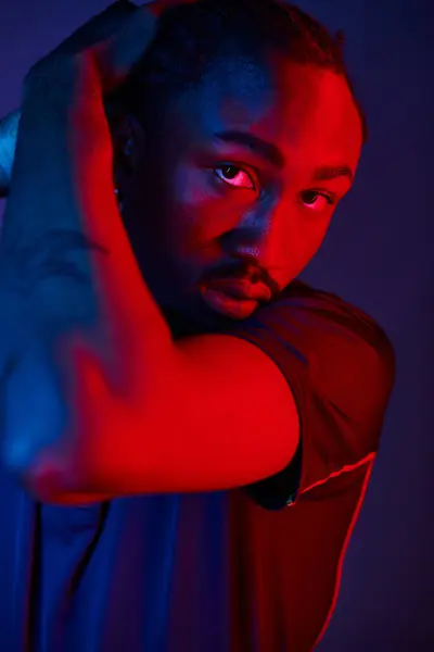 A young African American man showcases his stylish outfit while striking a dynamic pose in a neon-lit studio. — Stock Photo