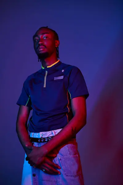 A young man with a striking style stands boldly in a studio illuminated by colorful neon lights, exuding charisma. — Stock Photo