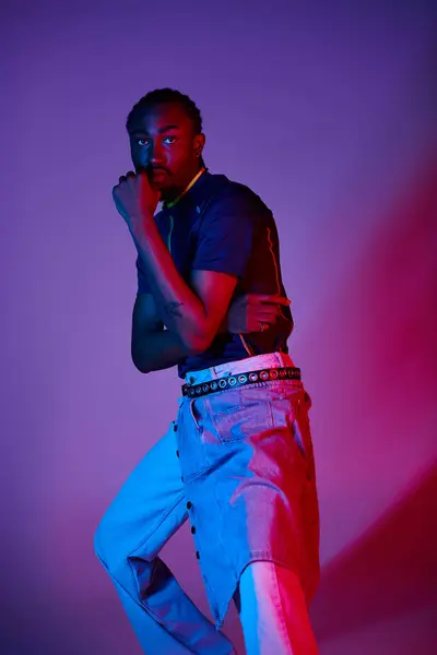 A young African American man showcases his stylish attire under striking neon lights, exuding confidence. — Stock Photo