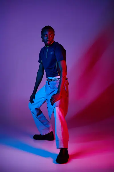 A young man confidently poses in trendy clothes, with vibrant neon lights enhancing the studio atmosphere. — Stock Photo