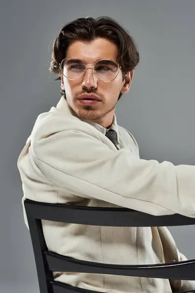 A young, handsome man in stylish formal attire poses confidently against a sleek grey backdrop. — Stock Photo