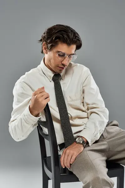 Un giovane in abito formale alla moda colpisce una posa pensierosa mentre seduto su uno sfondo grigio. — Foto stock