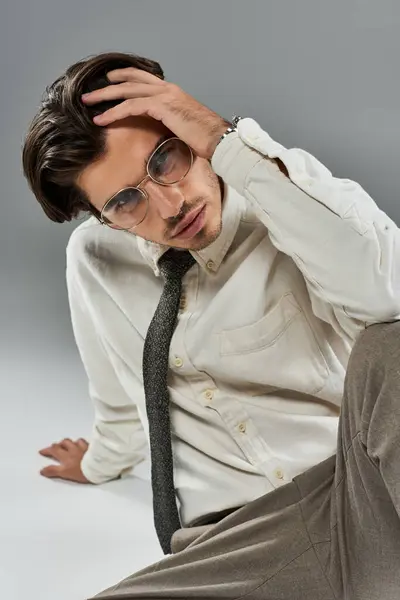 Un joven en ropa formal elegante se sienta en una pose contemplativa, exudando estilo y sofisticación en un estudio. - foto de stock
