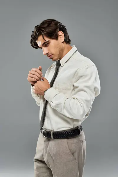 A young man dresses elegantly in a formal outfit, adjusting his tie while standing in a studio. — Stockfoto