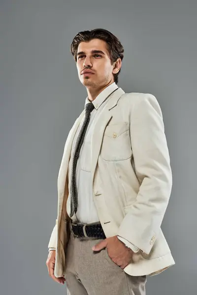 A young handsome man stands proudly in formal wear, his stylish look enhanced by a grey studio background. — Stock Photo